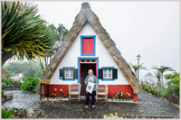 A somewhat bedraggled Carole with STA bag outside a traditional Madeiran thatched cottage