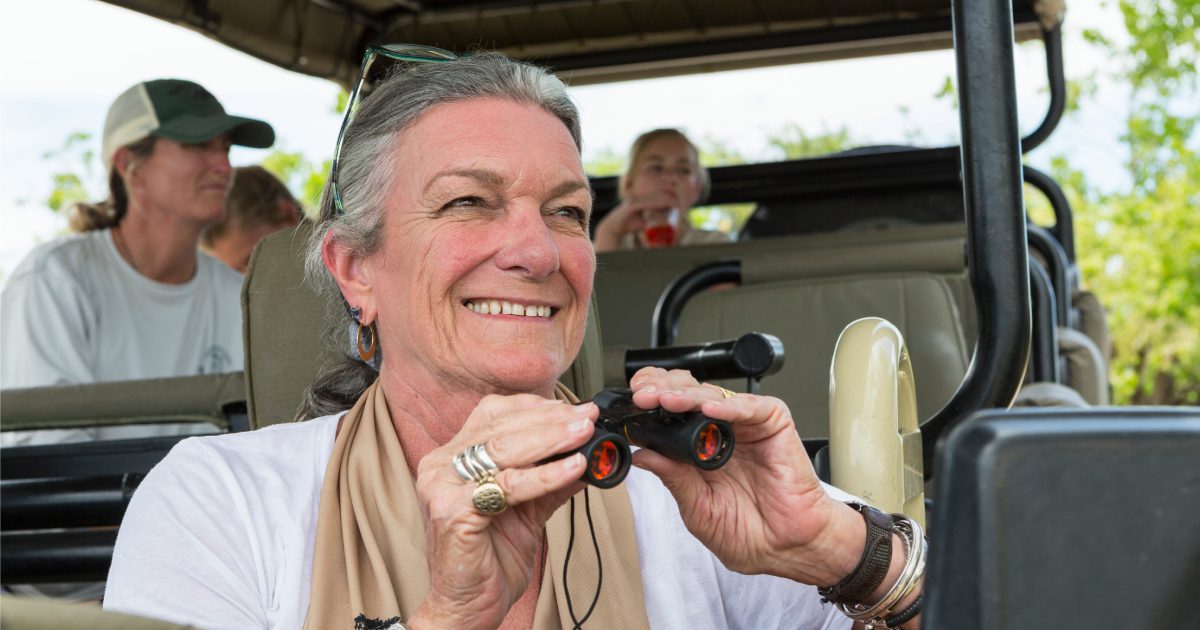 A family in a safari jeep in a wildlife reserve, a seniorwoman with binoculars. | Adventurous Safari